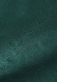 Material de culoare verde închis, cu o suprafață netedă și texturată, având un model de cusătură diagonală de-a lungul unei margini.