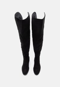 Musta pitkävartinen saapas pehmeää mokkaa. Ominaista on sulava pinta, muotoiltu varsi ja huomaamattomat saumat. Ei näkyvää metalliosaa.