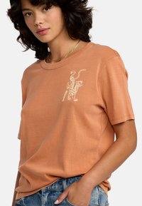 Katoenen T-shirt in gedempt terracotta met korte mouwen, ronde hals en een witte tijgerafbeelding gedrukt aan de linkerkant.