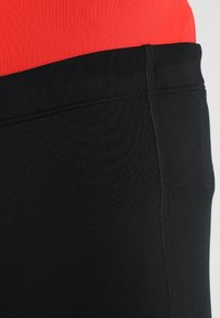 Černé sportovní šortky s hladkým povrchem, s kontrastním červeným horním páskem. Švy jsou viditelné podél okrajů.