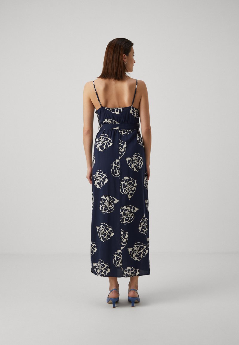 Robe maxi navy avec un motif floral blanc. Elle présente des bretelles spaghetti réglables, une taille ajustée et une silhouette fluide.