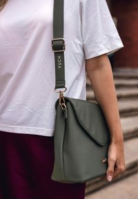 Olivově zelená crossbody taška z veganské kůže s klopou, nastavitelným popruhem se značkovým logem "VUCH" a zlatými kovovými akcenty.