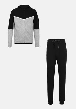 Vyriškas juodas ir pilkas su užtrauktuku užsegamas džemperis su chevrono raštu, derinamas su juodomis laisvalaikio kelnėmis, kurių liemuo su raišteliu, o kulkšnys surišti.