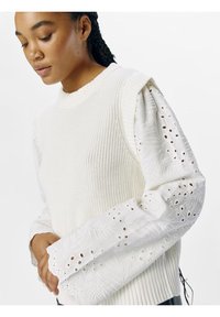 Maglione bianco lavorato a maglia con corpo testurizzato, caratterizzato da maniche ricamate bianche a palloncino con motivi floreali intagliati e orlo a coste.