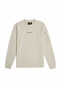 Jasno beżowa, długorękawowa koszulka wykonana z teksturowanej tkaniny, z okrągłym dekoltem i kieszonką zapinaną na zamek błyskawiczny na lewym rękawie. Logo nadrukowane centralnie.