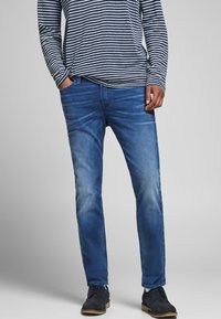 Blå denimjeans med slim fit, som har en urtvättad textur och subtila slitningar. Matchas med en randig skjorta med långa ärmar.