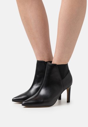 Bottines en cuir noir avec un bout pointu, une cheville ajustée et un talon haut et fin. Dotées de panneaux latéraux élastiques pour un enfilage plus facile.