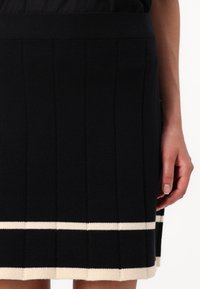 Black knit skirt with a fitted waistband, featuring vertical seams and a contrasting white stripe near the bottom hem. Soft texture.