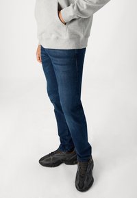 Dark blue jeans with a slim fit, paired with a gray sweatshirt. The jeans have a smooth texture, and the shoes are black with a mesh design.
