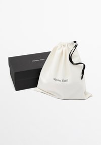 Sacchetto in cotone con coulisse color crema con la scritta "Massimo Dutti" stampata. Scatola rettangolare nera con testo corrispondente e finitura opaca.