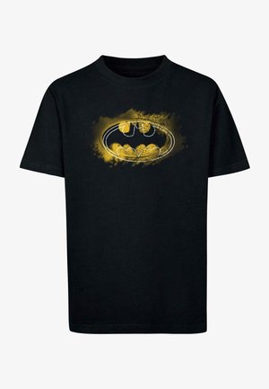 Camiseta de algodón negra con un logotipo de Batman en amarillo y blanco sobre un fondo texturizado. Diseño de manga corta y cuello redondo.