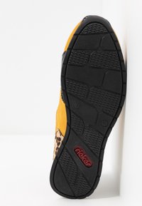 Semelle d'une chaussure jaune avec une bande de roulement noire, détail imprimé léopard sur le côté et logo rouge "rieker" sur la semelle.