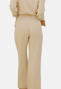 Pantalons larges beige à taille élastique fabriqués en tissu doux. Présente une texture lisse et un design minimal sans motifs visibles.