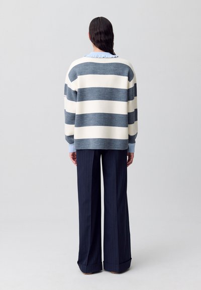 Maglione a righe in blu navy e crema, con ampie righe orizzontali. Abbinato a pantaloni larghi a righe verticali blu navy e un colletto azzurro.