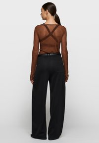 Top marrón translúcido de manga larga con un diseño sutil y cruzado en la espalda, combinado con pantalones negros sueltos que cuentan con un bolsillo lateral.