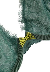 Soutien-gorge en dentelle verte avec un motif floral texturé, doté d'une bande inférieure vert foncé et d'un accent nœud jaune. Finition délicate le long des bords.