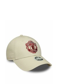 Beige Baseballcap mit rotem gesticktem Wappen von Manchester United auf der Vorderseite und einem gebogenen Schild mit einem silbernen Aufkleber obendrauf.