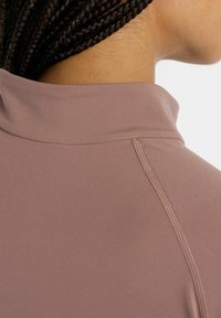 Top a maniche lunghe in tessuto mauve con colletto alto, cuciture testurizzate e finitura liscia, che enfatizza un design minimalista.