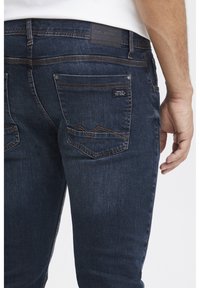 Mörka denimjeans med rak skärning, med orange sömmar på bakfickorna och en svart märkesetikett ovanför midjan.