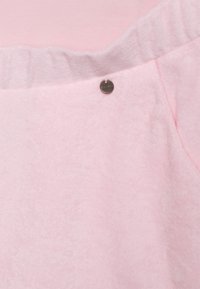 Tecido rosa claro com uma superfície suave e texturizada. Possui uma cintura elástica e um pequeno destaque metálico. Design simples e minimalista.