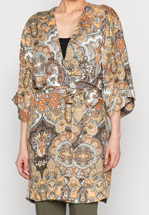 Vrouw die een wikkeljurk draagt met een paisleypatroon in oranje, bruin en wit, met driekwart mouwen en een gestrikte tailleband.