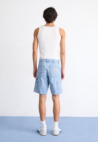 Pantalones cortos de mezclilla azul claro tipo cargo con múltiples bolsillos, combinados con una camiseta sin mangas blanca y zapatillas ligeras, vistos desde la parte posterior.