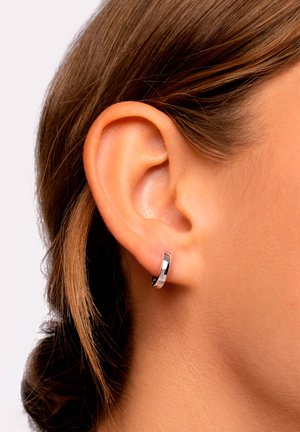 Boucle d'oreille en argent avec une finition polie, présentée sur l'oreille d'un modèle, mettant en valeur un design élégant et arrondi sur un fond neutre.