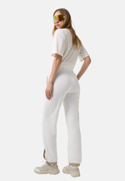 Hvid bomulds T-shirt og matchende sweatpants med en glat tekstur. Modellen bærer overdimensionerede gyldne solbriller og chunky beige sneakers.