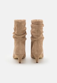 Bottines en daim beige à design décontracté, bout pointu et talon de 5 cm. Texture lisse avec des détails de coutures discrètes.