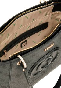 Borsa nera con esterno testurizzato e dettagli in oro. Interno con rivestimento beige e stampa del logo verde "GUESS" e numerosi scomparti.