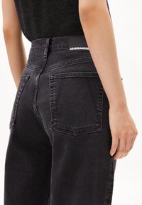 Black denim jeans with a high waist, featuring a back pocket design, visible stitching, and a branded patch at the waistband.