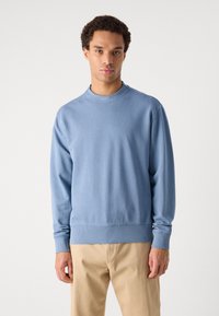 Ανοικτό μπλε φούτερ με στρογγυλή λαιμόκοψη, ριμπ μανσέτες και σάκο, κατασκευασμένο από μαλακό υλικό. Διαθέτει ένα μικρό λογότυπο κοντά στη λαιμόκοψη.