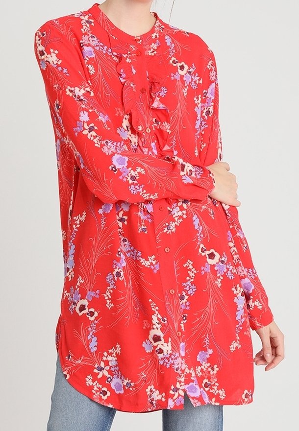 Blouse florale rouge à manches longues, avec un devant à volants et une fermeture à boutons. Présente des fleurs violettes et blanches sur un fond texturé.
