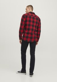 Chemise en flanelle à carreaux rouge et noir, à manches longues, avec des poignets boutonnés et un ourlet droit, associée à un pantalon noir et des baskets noires.