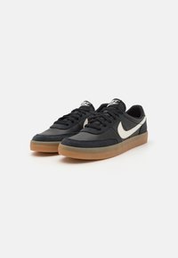 Baskets noires avec un mélange de cuir lisse et de daim texturé. Présentent un logo swoosh blanc et une semelle en caoutchouc gomme. Design à lacets.