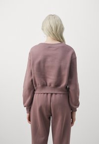 Överdimensionerad mauve sweatshirt med rund halsringning och ribbade ärmslut. Mjuk och bekväm tyg, med en figursydd midja och mjuk textur.
