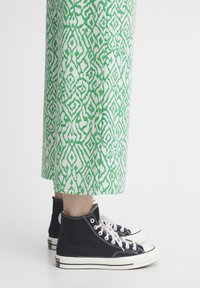 Gröna och vita mönstrade vida byxor med en geometrisk design, kombinerade med svarta canvas högklackade sneakers med vita sulor och snören.