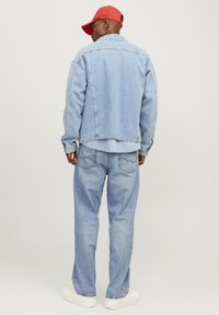 Lichtblauwe spijkerjack en bijpassende broek met brede pijpen. Witte sneakers. Rode baseballpet. Zichtbare stikdetails op de kleding.