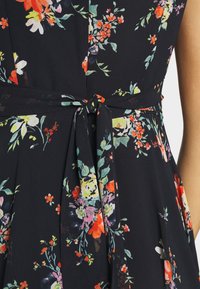 Robe fleuri en tissu marine avec des fleurs vives de couleur rose, orange et verte, dotée d'une ceinture à la taille et d'un design plissé froncé.