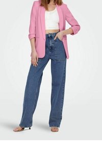 Blazer rosa con maniche rimboccate sopra una maglietta corta bianca, abbinato a jeans in denim blu a vita alta e gamba larga e sandali con tacco nudo.