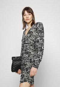 Vestido impresso em preto e branca com decote profundo, mangas longas e textura franzida, combinado com uma bolsa de mão acolchoada preta.