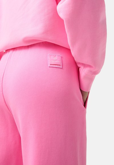Rosa Sweatshirt und passende Jogginghose aus weichem Material. Mit einem quadratischen Logopatch am hinteren Bund, der eine strukturierte Oberfläche hat.