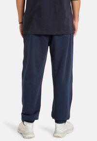 Navyblauwe katoenen sweatpants met elastische boorden en zakken, gecombineerd met lichtgekleurde sportschoenen. Zichtbare stiksels en een relaxte pasvorm.