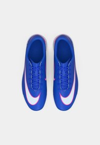 Kék szintetikus focicipők sima felülettel, kiemelkedő fehér Nike logóval, rózsaszín kiegészítőkkel és hagyományos fűzőzéssel.