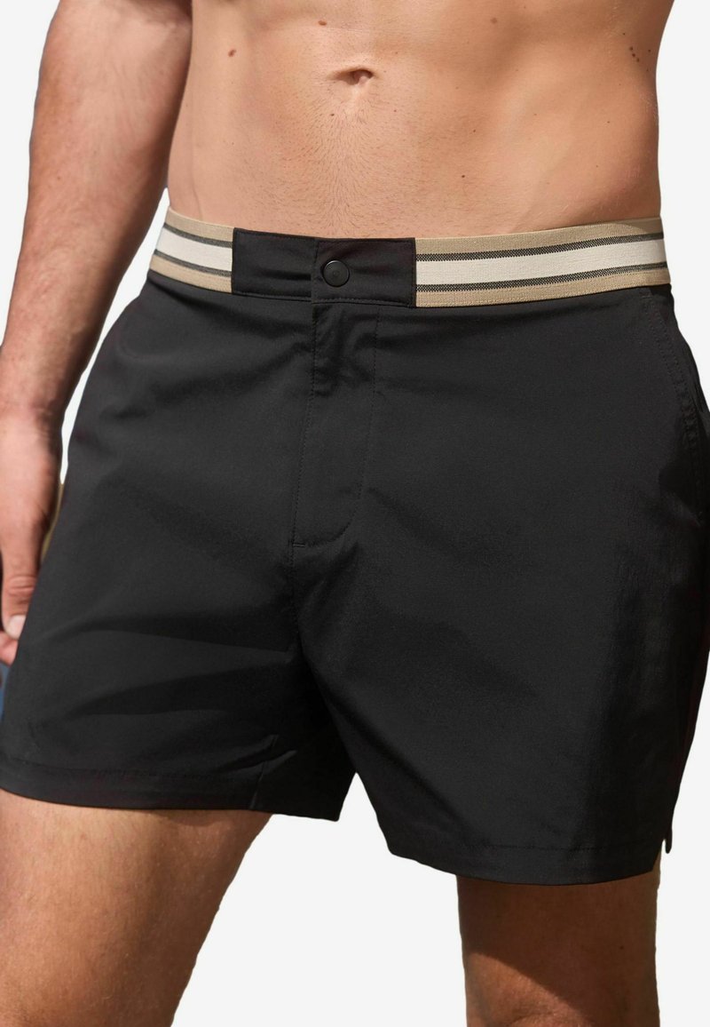 Shorts de bain noirs en tissu léger, dotés d'une ceinture élastique rayée beige et noire et d'une fermeture à bouton à l'avant.