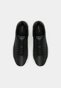 Adidaşi din piele neagră cu tălpi din cauciuc alb. Caracteristici includ vârf rotund, şireturi plate şi logo-ul brandului embosat pe limbă şi pe lateral.