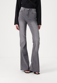 Aukštai taliją dengiančios pilkos flared džinsai, pagaminti iš džinsinio audinio, su klasikinio penkių kišenių dizainu ir subtilia tekstūra. Sukomplektuoti su juodais kulnais.
