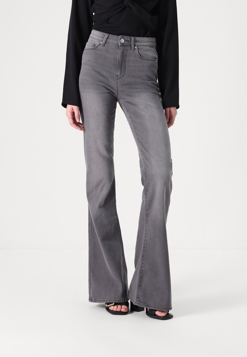 Aukštai taliją dengiančios pilkos flared džinsai, pagaminti iš džinsinio audinio, su klasikinio penkių kišenių dizainu ir subtilia tekstūra. Sukomplektuoti su juodais kulnais.