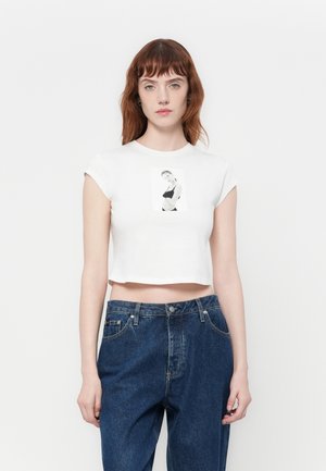 White cropped t-shirt with short sleeves featuring a black-and-white graphic print on the front. Paired with dark blue high-waisted jeans.