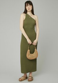Robe olive texturée à une épaule, associée à un sac en osier et des sandales à plateforme brunes. Fond neutre.